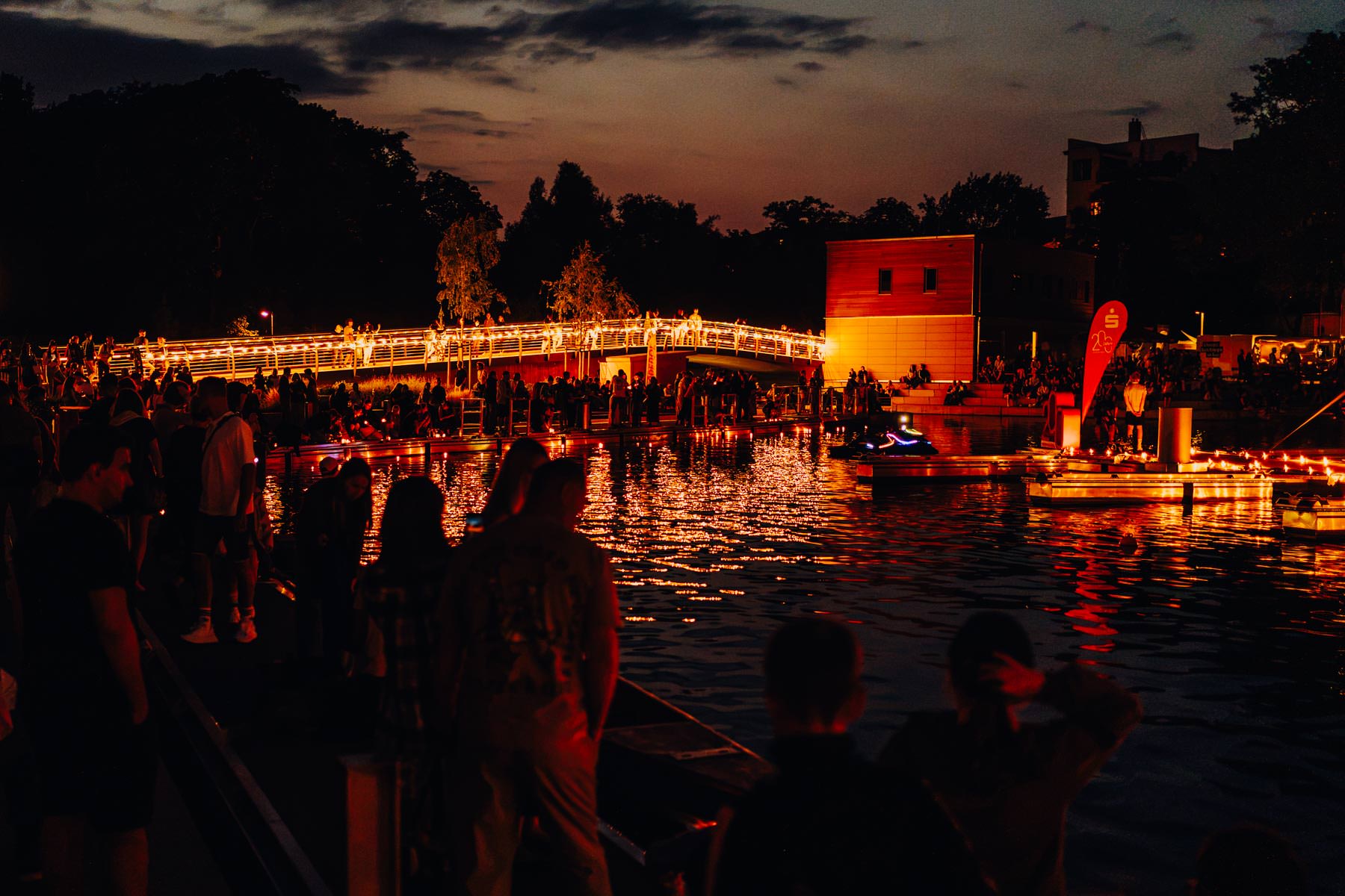 Eventfotograf Leipzig Abendstimmung Stadthafen Menschenmenge bei einer Abendveranstaltung zum Hafenfest im Stadthafen Leipzig mit beleuchteter Brücke und warmen Lichtreflexionen