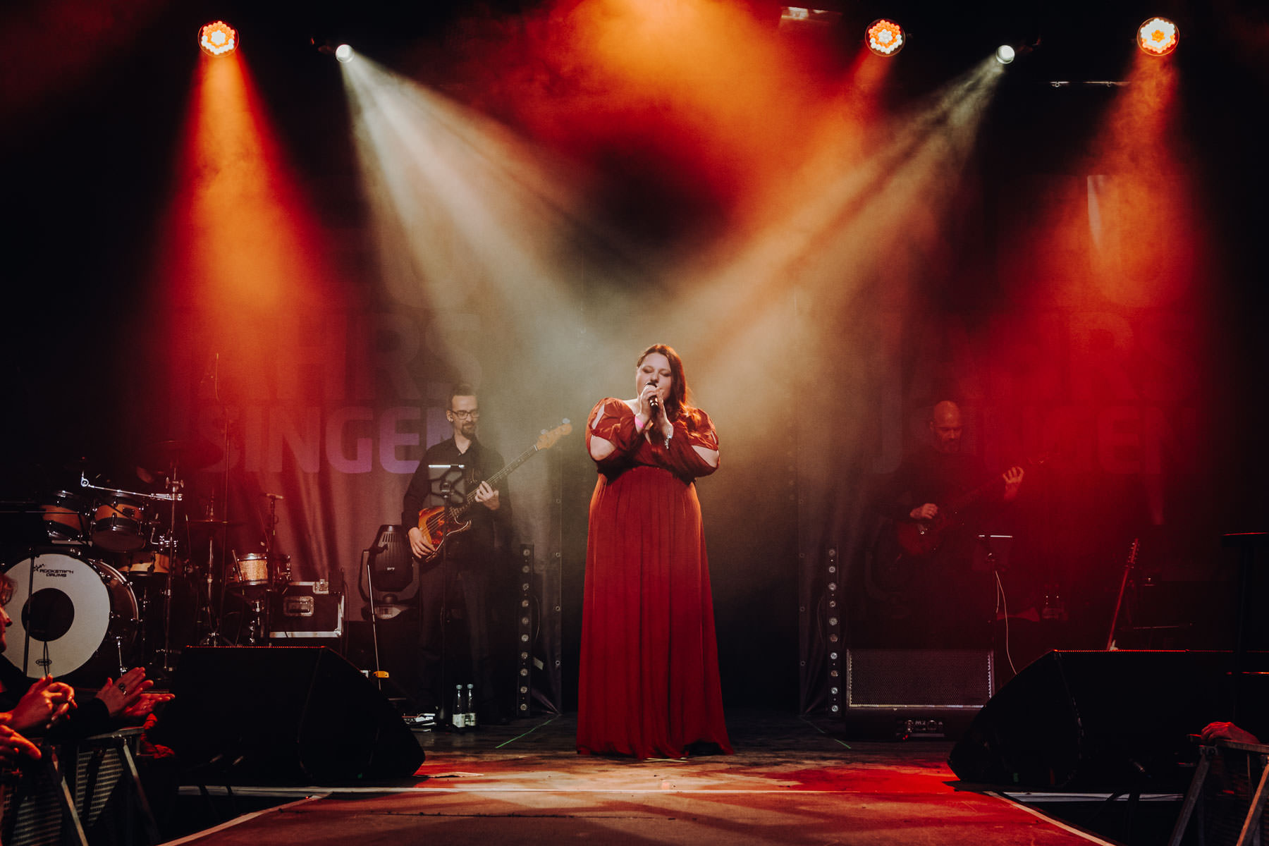 Eventfotograf Leipzig Neujahrssingen Felsenkeller Sängerin in rotem Kleid singt auf einer Bühne mit Band unter dramatischem Scheinwerferlicht im Felsenkeller zum Neujahrssingen