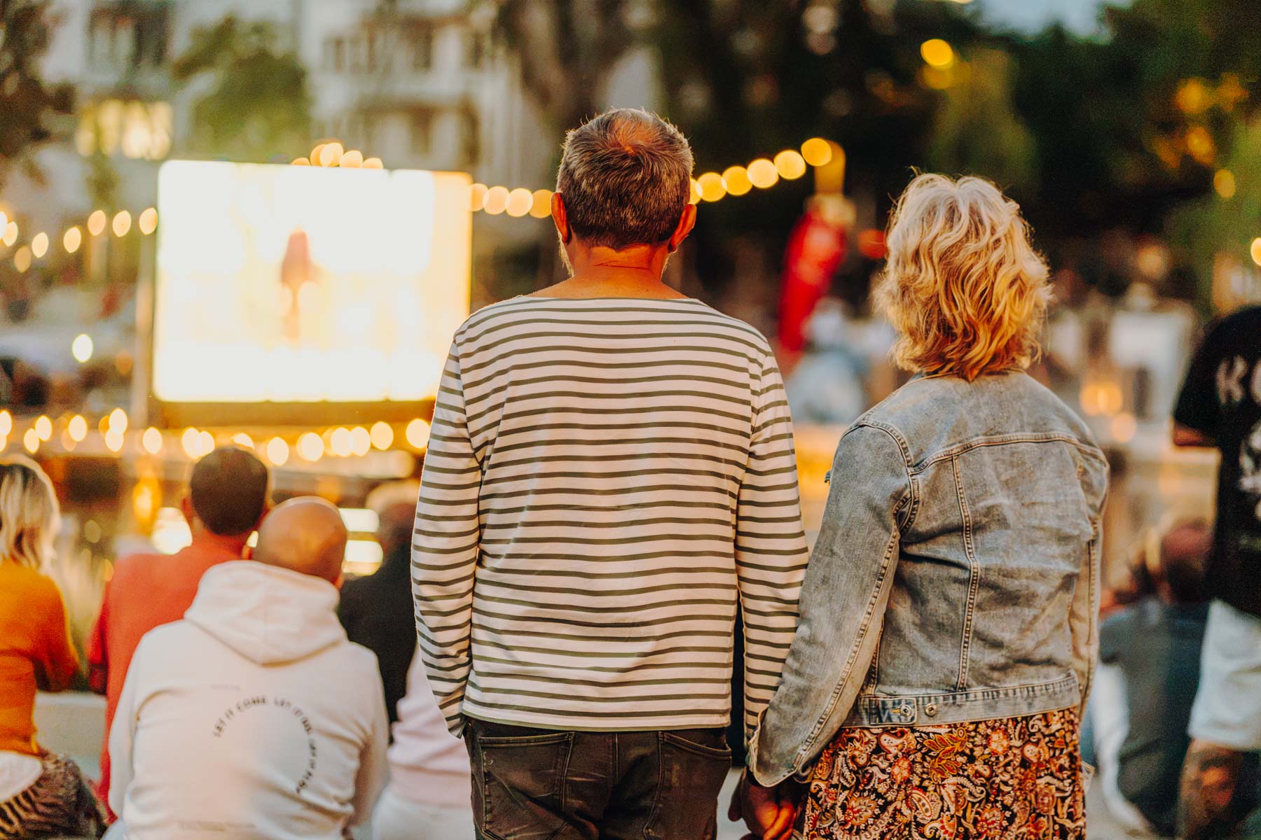 Eventfotograf Leipzig Sommerkino Hafenfest Ein Paar blickt auf eine Leinwand beim abendlichen Sommerkino mit Lichterketten im Stadthafen Leipzig